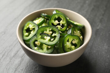 Pieces of green jalapeno peppers in bowl on grey table, closeup