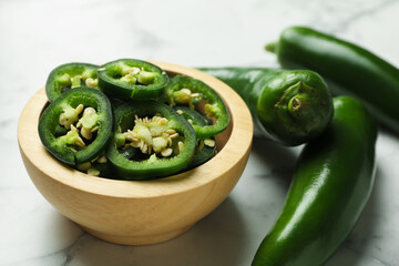 Whole and cut jalapeno peppers on white marble table, closeup