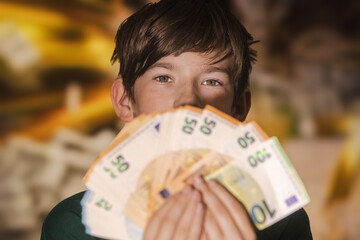 Smiling boy proudly holding a fan of euro banknotes in 20, 50, and 100 denominations, symbolizing wealth, savings, finance, and prosperity.