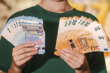 Smiling boy in a green shirt holding fans of 20 and 50 euro banknotes, symbolizing money, savings, wealth, finance, or success.