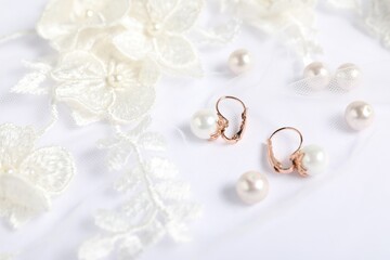 Beautiful earrings, pearls and lace fabric on white background, flat lay