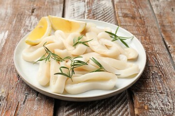 Uncooked squid rings with lemon slices and rosemary on wooden table, closeup
