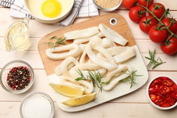 Uncooked squid rings, spices, yolk, bread crumbs and tomatoes on wooden table, flat lay