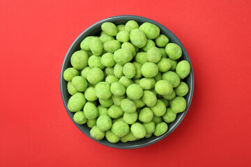 Delicious wasabi coated peanuts in bowl on red background, top view