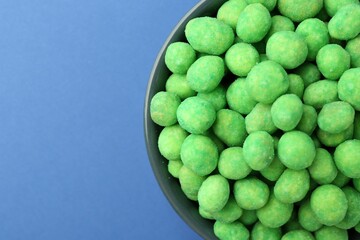 Delicious wasabi coated peanuts in bowl on blue background, top view. Space for text