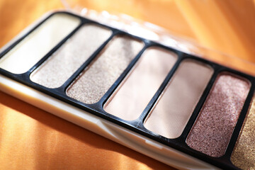 Colorful eyeshadow palette on orange background with shadows, closeup