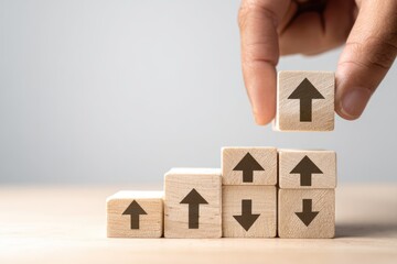 Human hand building a staircase of wooden blocks with arrows pointing upwards showing financial or personal growth