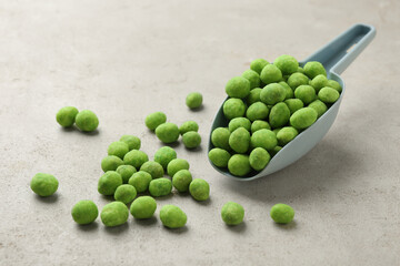 Delicious wasabi coated peanuts and scoop on grey textured table, closeup