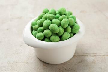 Wasabi coated peanuts in bowl on light table, closeup