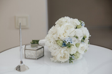 White wedding bouquet on table with ring box and pen