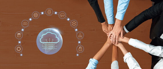 Diverse team collaborates above a wooden table, showcasing hands joining together with a digital cloud concept, symbolizing teamwork and data sharing in the modern workplace. Trope
