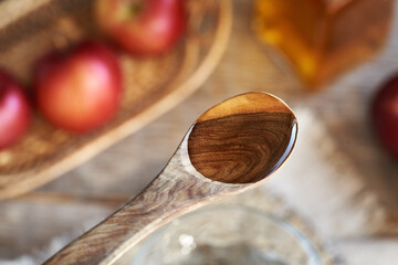 Apple cider vinegar on a wooden spoon with fresh apples in the background