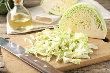 Cut fresh Savoy cabbage, knife and oil on wooden table, closeup