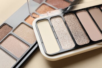 Beautiful eyeshadow palettes on beige background, closeup
