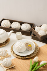 A serene setup featuring steamed buns with a filling, accompanied by a tea set and fresh tulips, creating a cozy dining atmosphere.