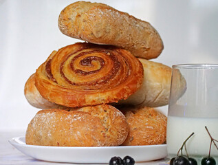 A Stack of Freshly Baked Cinnamon Buns with a Glass of Milk - some large cinnamon buns is served on a white plate next to a tall glass of milk. Classic, cozy breakfast perfect for a cold autumn 