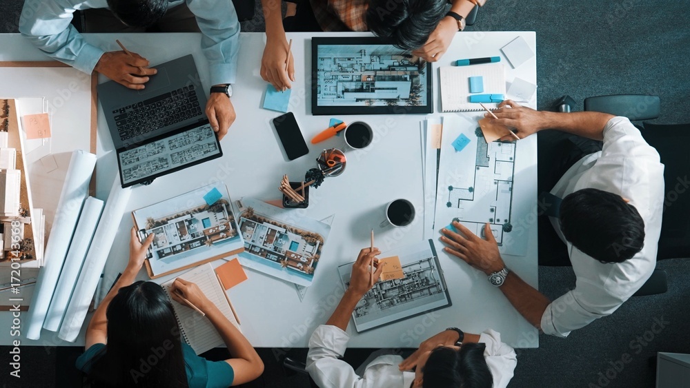 Poster top view of smart architect engineer writing at blueprint while sitting at meeting table with house 