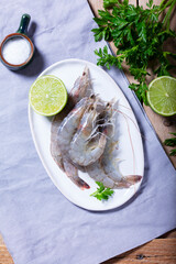 Fresh shrimp, lime, salt, and parsley on a ceramic plate on a wooden table.