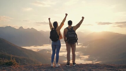 Couple reaching mountain peak, holding hands and raising arms in triumph, enjoying beautiful panoramic view of mountain ranges and morning fog under a bright sunrise sky