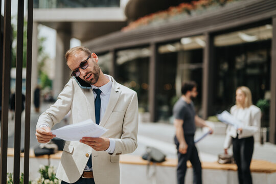 Businessman multitasking during a call, reviewing documents while managing tasks in a city environment.
