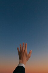 Reaching for the stars at dusk with a hand against a colorful sky