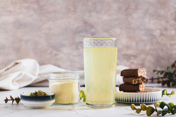 Matcha protein drink in a glass, powder and protein bars on table