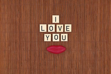"I love you" written on wooden blocks with a red lip-shaped candy isolated on a wooden background. Top view. Concept of love.