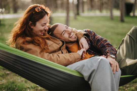 A cheerful couple enjoying leisure time in a hammock amidst the serene setting of nature. Capturing the charm of a special moment outdoors, embracing love, happiness, and a joyful connection.