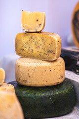 Stack of artisanal cheese wheels with herbs and spices. Traditional dairy product displayed at a market, symbolizing gourmet food, rustic cuisine, and authentic cheese-making