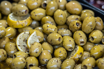 Close-up of marinated green olives with lemon slices and herbs. Traditional Mediterranean appetizer and snack, seasoned with spices and olive oil. Fresh and healthy gourmet food