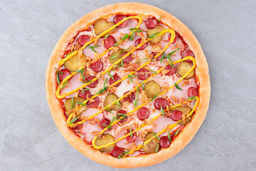 Cheeseburger Style Pizza with Pickles, Sausage, Ham, Mustard Drizzle, Fried Onions, and Green Onions on Golden Crust over Gray Stone Background