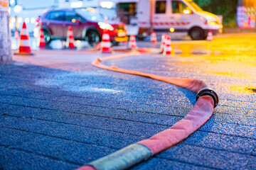 Fire hose on wet road with red cars and rescue unit nearby