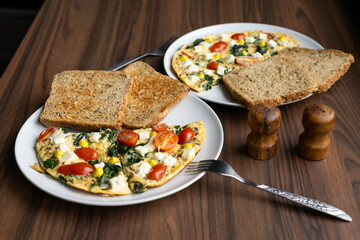 Omelette with tomatoes, spinach, cheese, and toast on white plate