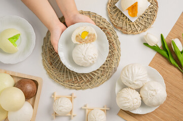A person holds a plate with steamed buns, showcasing various flavors and styles, surrounded by decorative elements and fresh tulips.