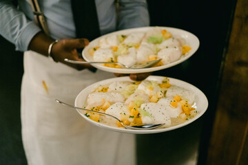 Server carries two plates of fresh fish dishes with garnishes in a busy restaurant setting