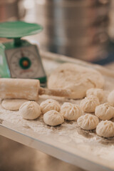 A collection of freshly made dumplings alongside a rolling pin and a scale, set on a flour-dusted surface in a well-lit kitchen.