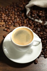 Aromatic coffee in cup and beans on wooden table, closeup