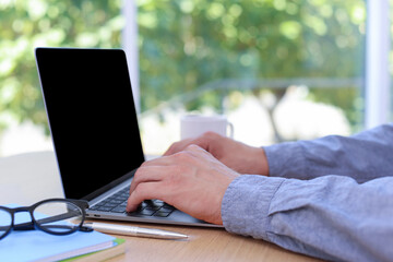 Fototapeta premium Man working on laptop at wooden table indoors, closeup
