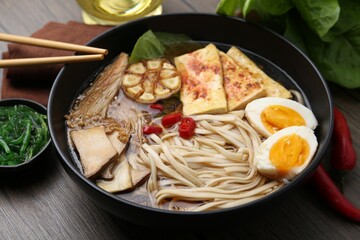 Tasty ramen with enoki and king oyster (eryngii) mushrooms in bowl on wooden table, closeup