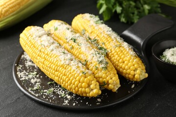 Tasty grilled corncobs with parsley and cheese on black table, closeup