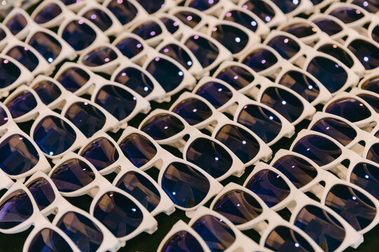 Large collection of stylish white sunglasses displayed in a market setting under bright lighting