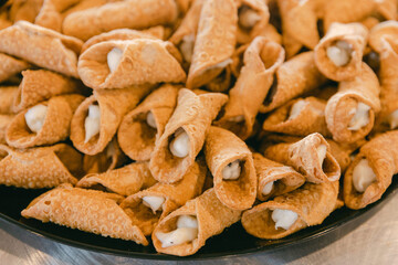 Delicious homemade cannoli filled with sweet cream displayed on a black platter at a festive gathering