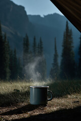 coffee cup sits invitingly in front of tent framed by majestic mountains and serene forest