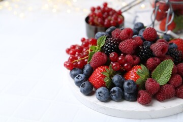 Different ripe berries and mint leaves on white tiled table, closeup. Space for text