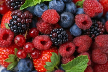 Different ripe berries and mint leaves as background, above view