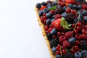 Different ripe berries in wicker basket on white tiled table, closeup. Space for text
