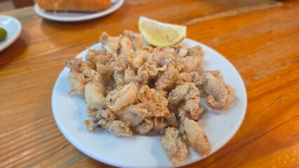 Crispy fried calamari with lemon on rustic wooden table setting. Traditional Spanish dish