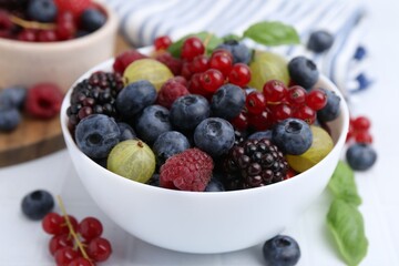 Different ripe juicy berries and basil in bowl on white tiled table, closeup