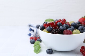 Different ripe juicy berries in bowl on white tiled table. Space for text