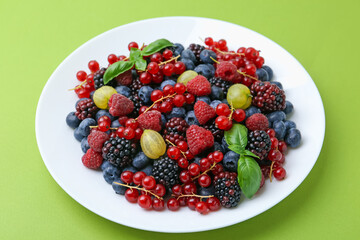 Different ripe juicy berries on plate against green background, closeup